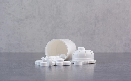 Белые таблетки рассыпаны из пластиковой баночки на сером столе